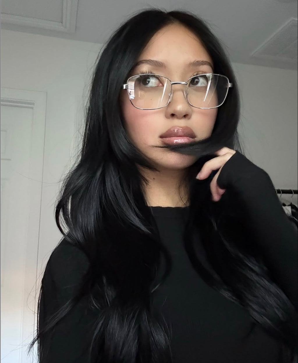 Woman with long black hair and metal cat eye glasses taking a selfie indoors