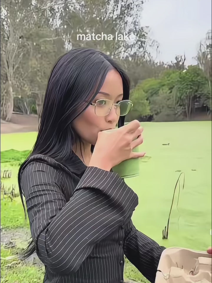 A woman in metal cat eye frames drinking matcha from a lake 